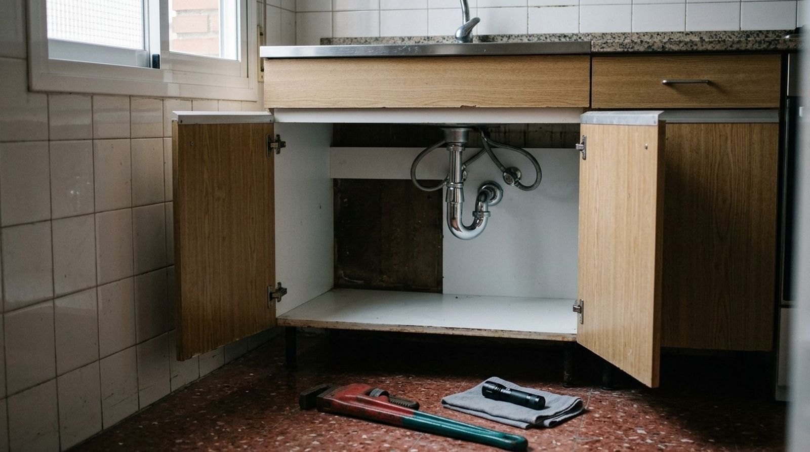 Tubería y sifón nuevos bajo el fregadero de una cocina, con el mueble abierto