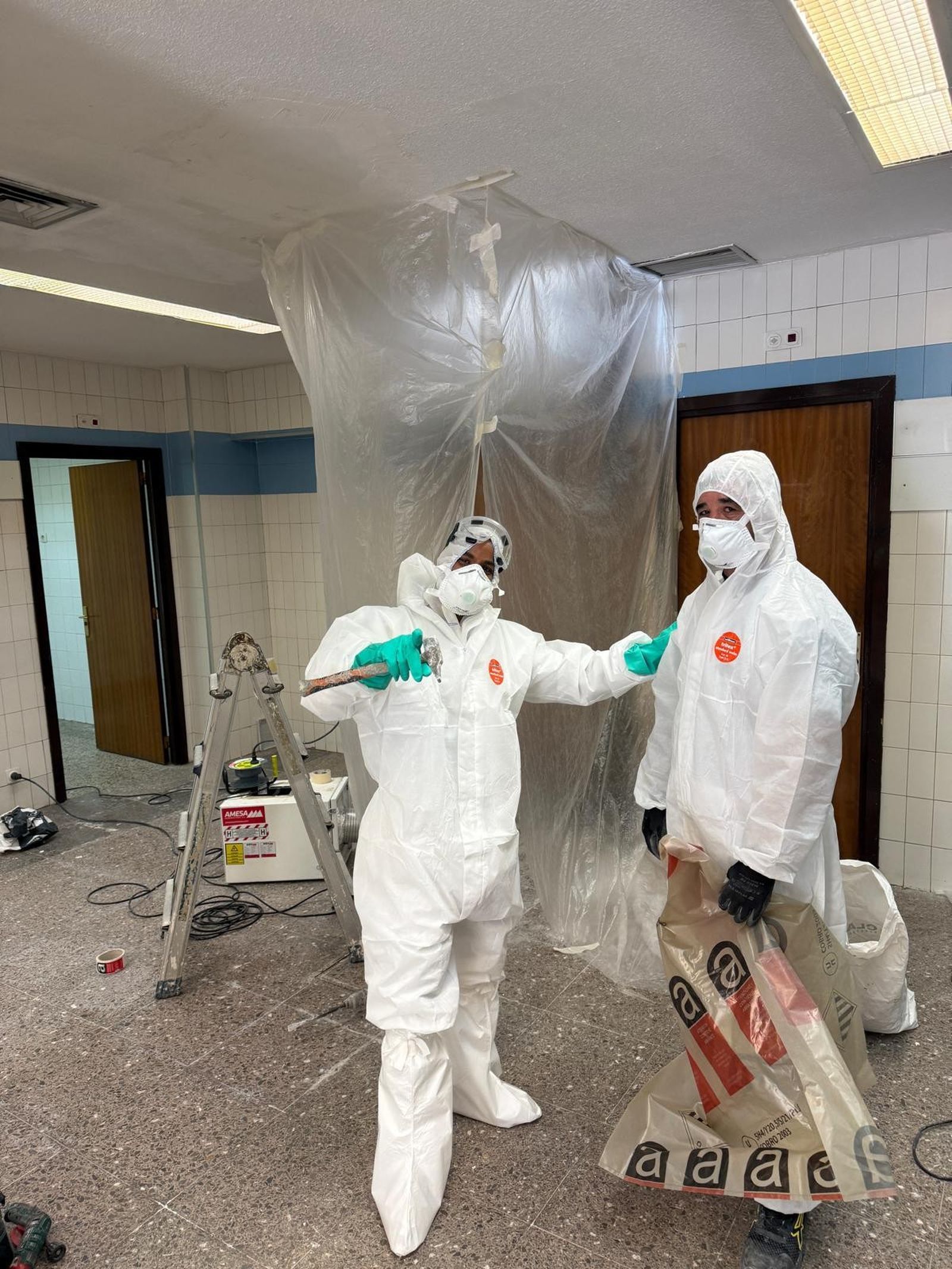 Dos operarios de Solvento con mono, mascarilla y guantes junto a la zona de trabajo cerrada con plástico